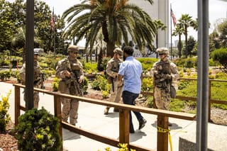 A group of four U.S. Marines wearing military gear and holding guns watch a civilian walk past them near the Wilshire Federal Building in Los Angeles, California.