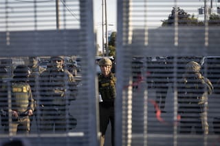 U.S. Border Patrol Commander Gregory Bovino, wearing a helmet, stands with masked border patrol agents behind a gate in Broadview, Illinois.