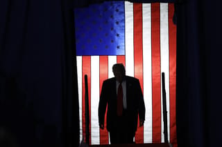 President Donald Trump, silhouetted against the American flag, climbs the stage to speak during a rally on April 29, 2025.