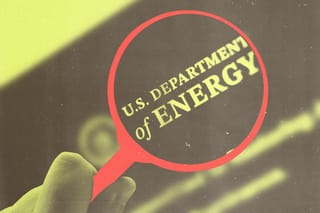 A hand holds a magnifying glass over the U.S. Department of Energy logo