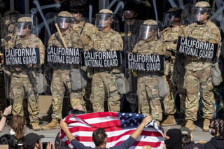 California National Guard soldiers wear riot gear and hold shields in front of a crowd of protesters in Los Angeles, California, June 9, 2025.