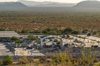 Wide shot taken from an elevated view of Ajo Border Patrol Station in late afternoon. The station is surrounded by barren desert scrub with low mountains in the distance.