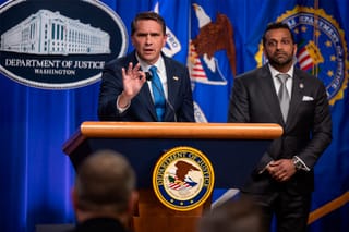 Acting Attorney General Todd Blanche speaks to a member of the press from a podium at the Department of Justice with FBI Director Kash Patel standing behind him.