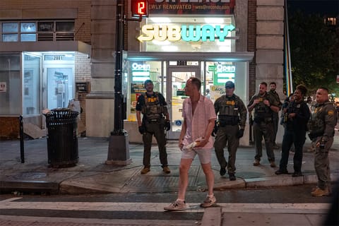 Sean Dunn, in the foreground, holds a sandwich and appears to walk away from a group of federal agents on a sidewalk in Washington, DC.