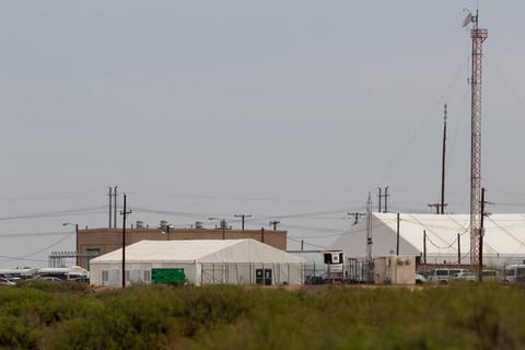 Two soft white tent facilities in the distance surrounded by a fence mark Camp East Montana in El Paso, Texas.