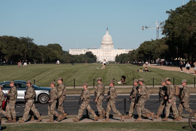 In front of the U.S. Capitol building, National Guard soldiers hold weaponry while patrolling the National Mall.