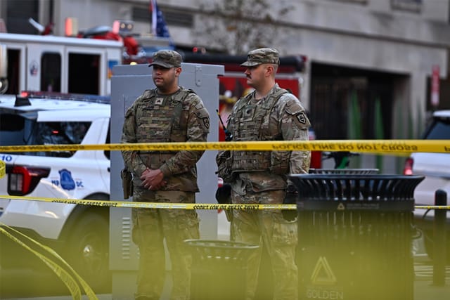Two U.S. National Guard members stand behind yellow police line tape in Washington, DC.