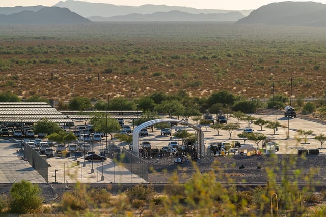 Wide shot taken from an elevated view of Ajo Border Patrol Station in late afternoon. The station is surrounded by barren desert scrub with low mountains in the distance.