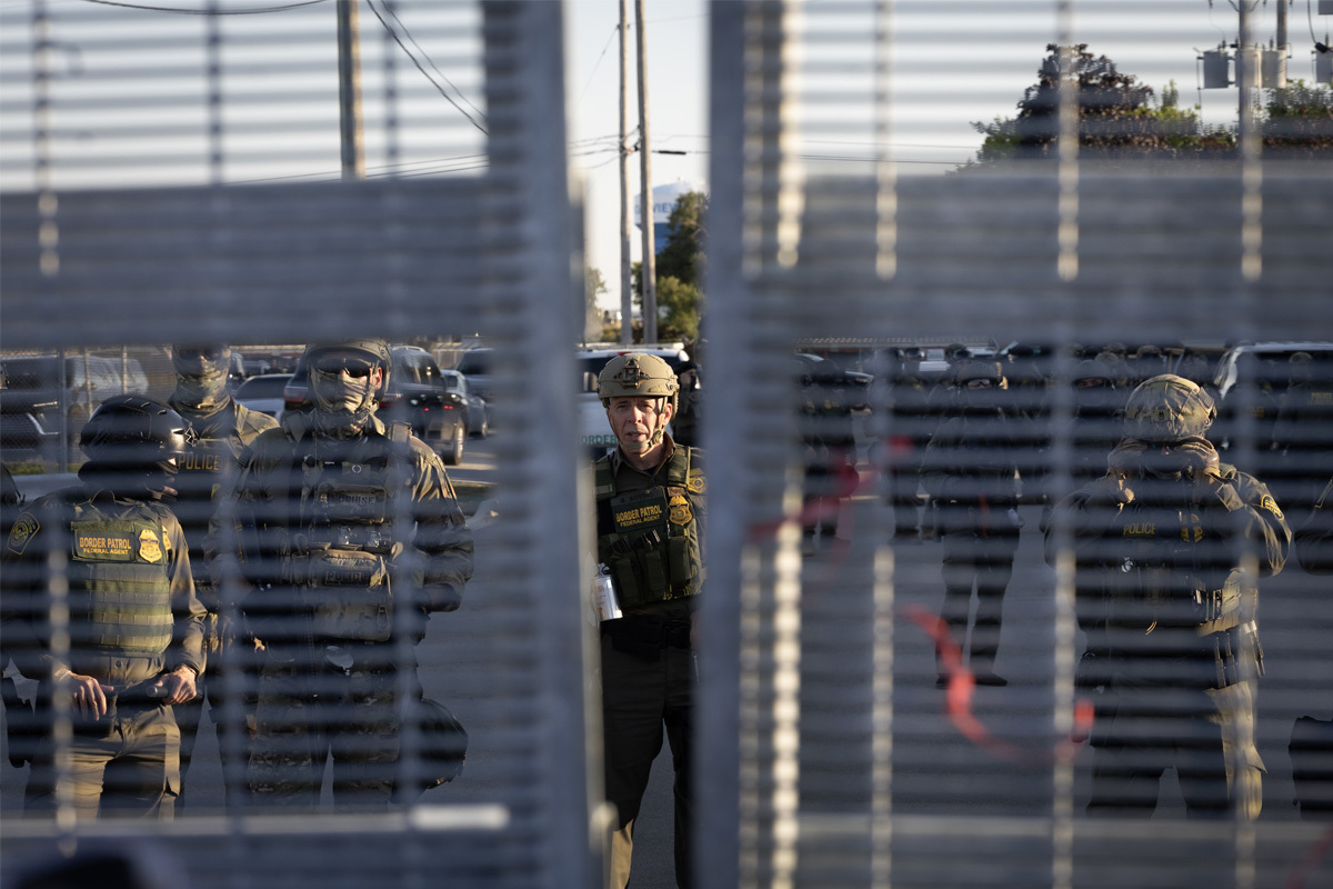 U.S. Border Patrol Commander Gregory Bovino, wearing a helmet, stands with masked border patrol agents behind a gate in Broadview, Illinois.